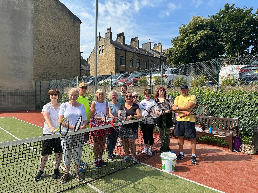 Group of walking tennis participants posing behind the net on a tennis court.
