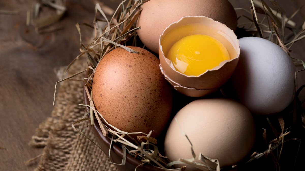 Brown and white eggs in a bowl, one cracked open showing yolk.