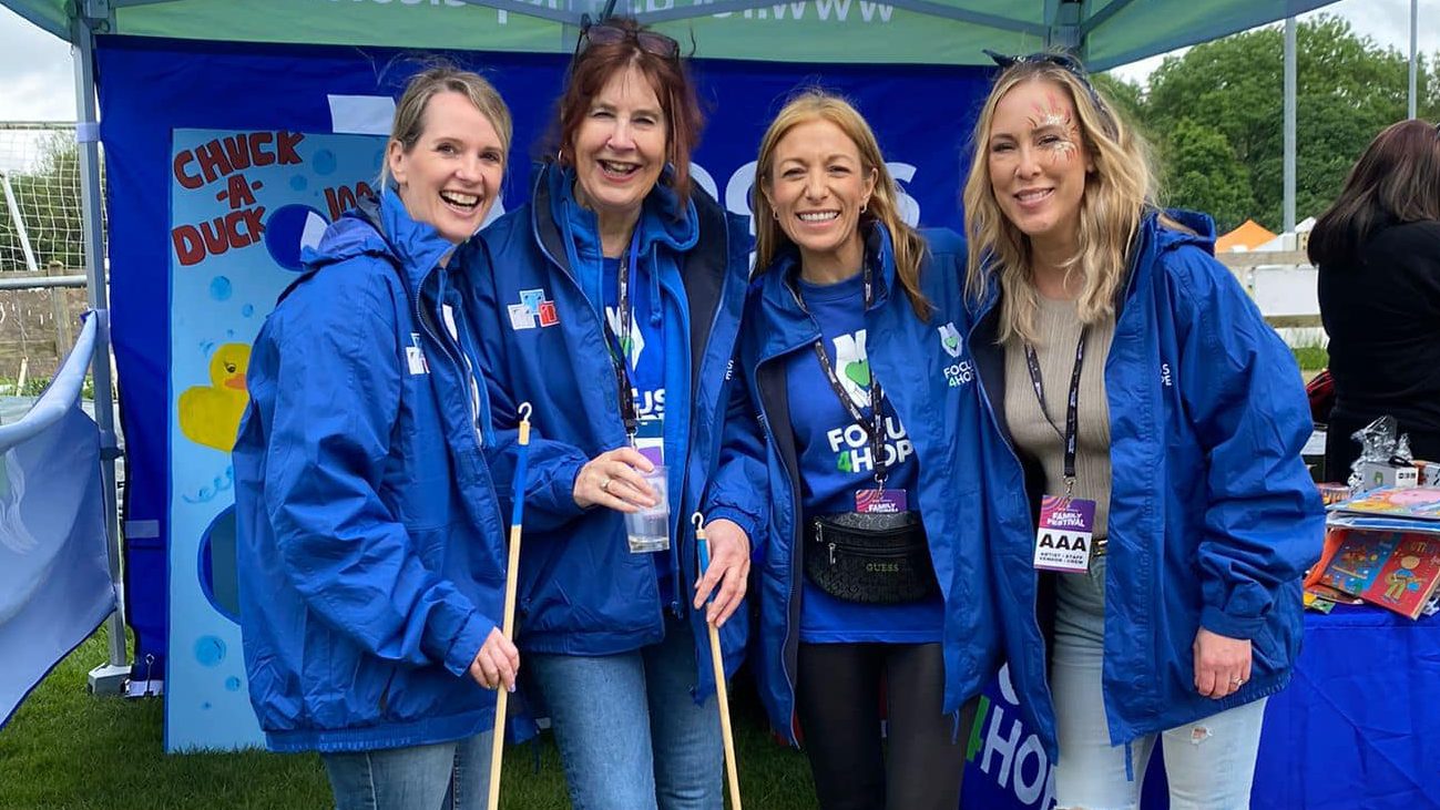 Four Focus4Hope volunteers wearing blue jackets stand smiling under a branded canopy at an outdoor event.